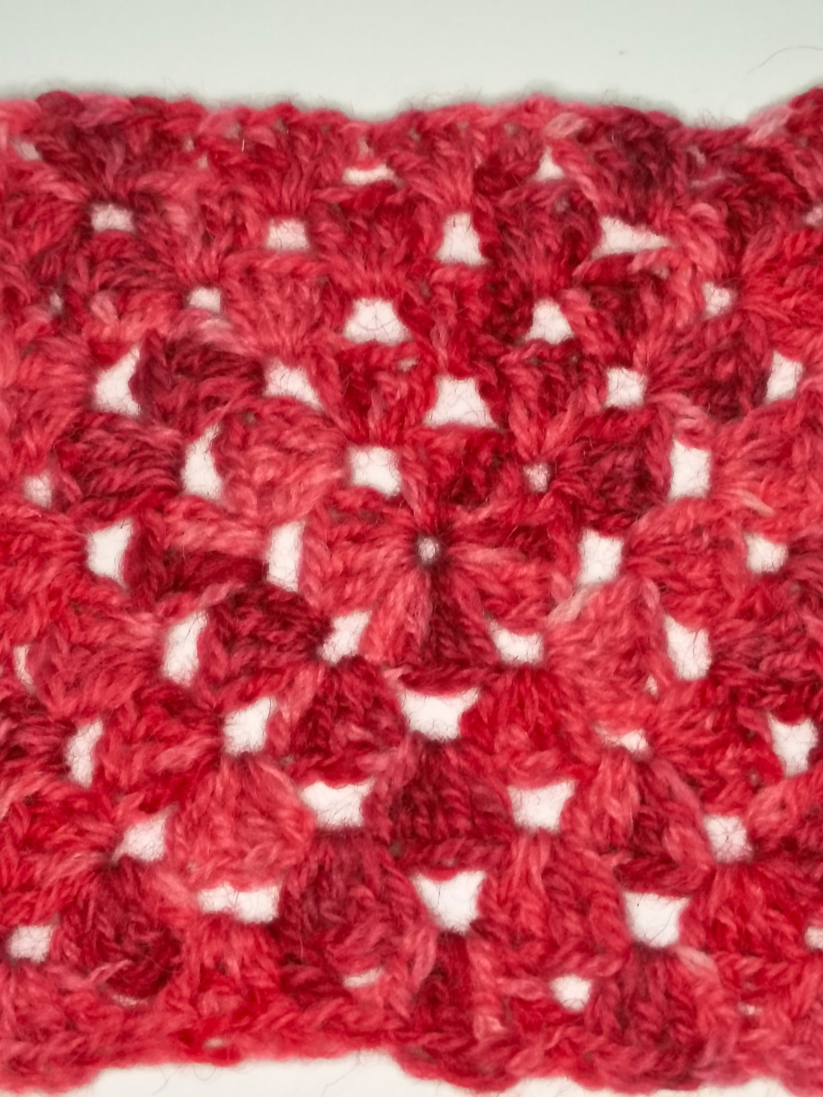 A close-up red swatch showing a textured granny square pattern with openwork details.
