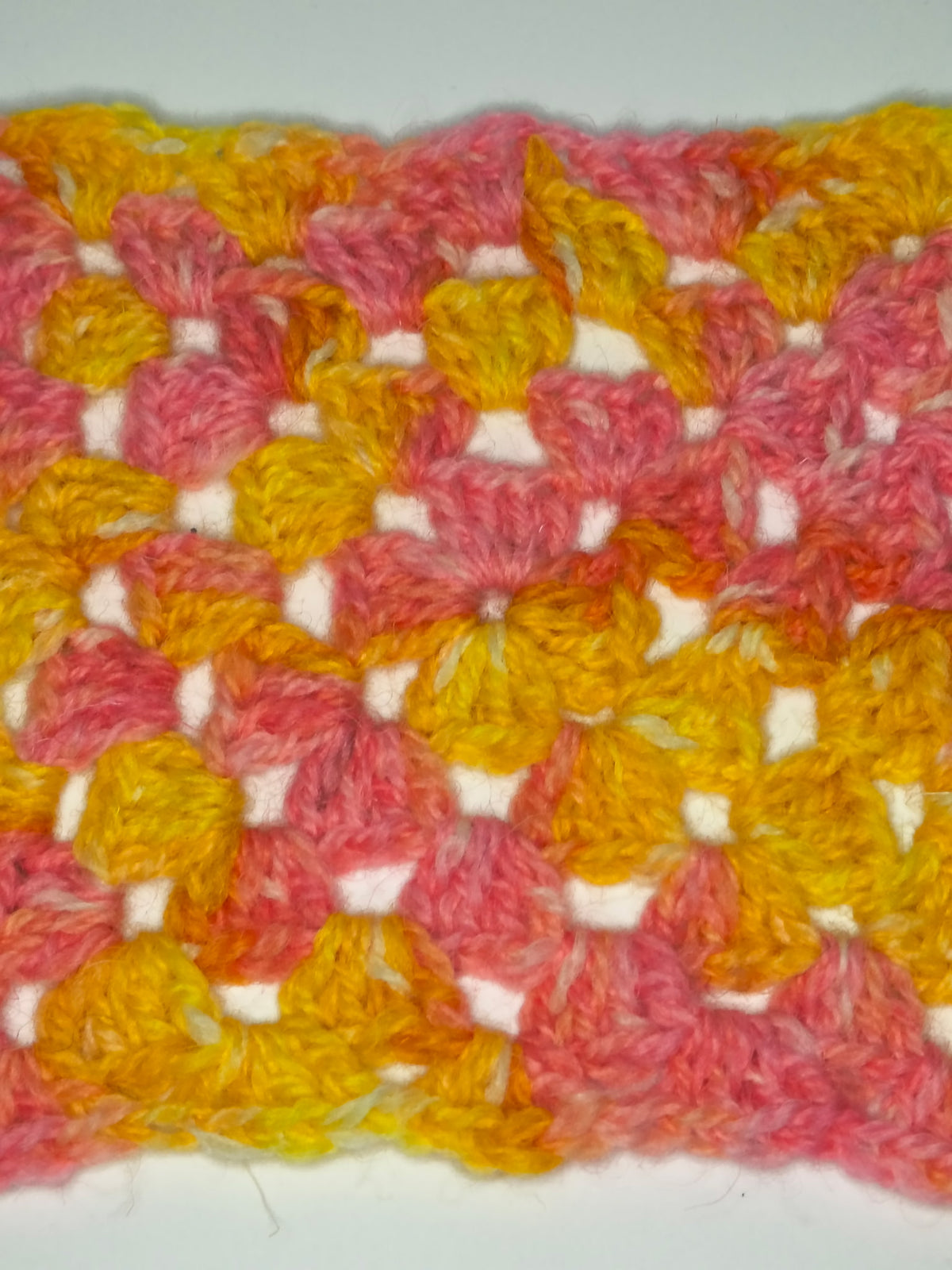 A close-up swatch with a textured floral pattern in pink, orange, and yellow yarn on a white background.